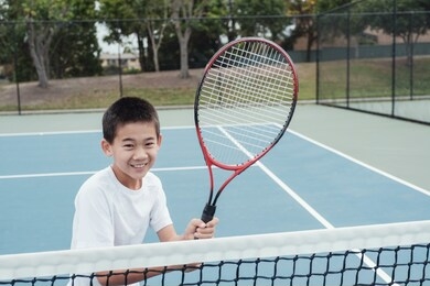 young tween asian boy tennis beginner player on outdoor blue court