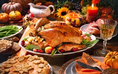 thanksgiving dinner. roasted turkey garnished with cranberries on a rustic style table decoraded with pumpkins, vegetables, pie, flowers and candles