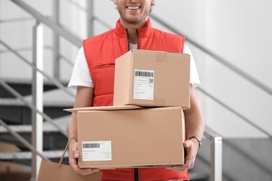 young courier standing with parcels near stairs indoors