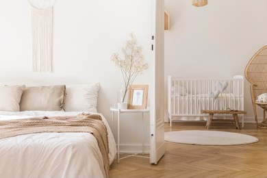 white metal bedside table with decor and coffee mug placed by the bed in bright bedroom interior with door to newborn baby room with crib