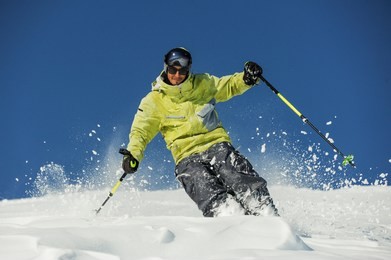 happy skier dressed in bright yellow sportswear riding down the mountain slope in georgia, gudauri on sunny day