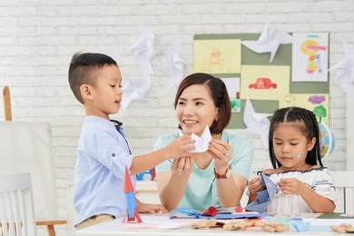 young asian woman teaching children how to make paper ships at art craft