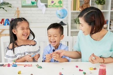 laughing children and teacher making toys out of playdough