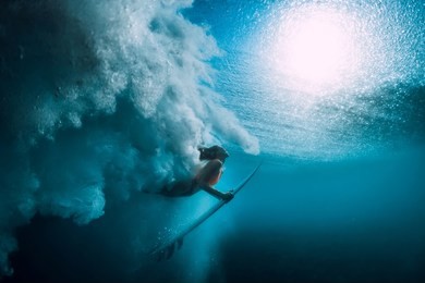 surfer girl with surfboard dive underwater with under big ocean wave.