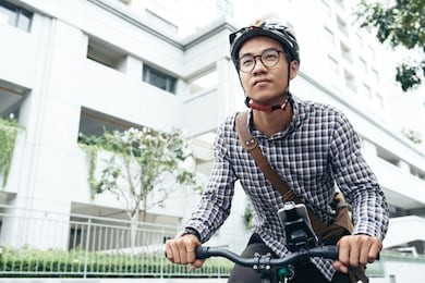 young good-looking asian man wearing safety helmet and glasses looking forward while riding bicycle to work