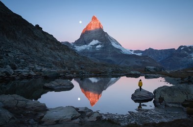 a girl on a rock in the riffelsee watching the first sunlight on the matterhorn.