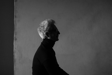 never get old, handsome and sexy at every age concept. portrait of fashionable mature man wearing trendy eyewear, black turtleneck, sitting in art gallery. modern haircut. silver hair. graphic shadows
