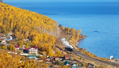lake baikal. view of the circum-baikal railway from above on an autumn day. tourist excursion historic locomotive arrives in the village of kultuk. tourists take pictures of the train