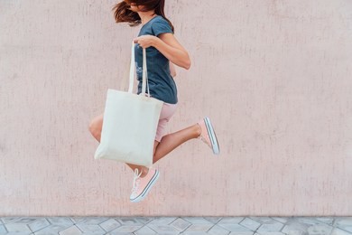 young woman is jumping with white cotton bag in her hands.