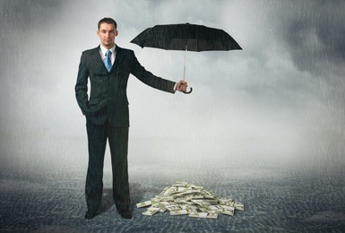 businessman with umbrella stands at cloudy background and protects a money. financial safety