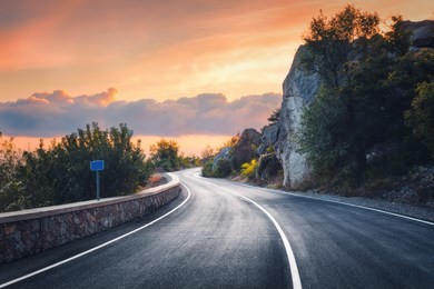 mountain road at sunset. landscape with rocks, orange sunny sky with clouds and beautiful asphalt road in the evening in summer. vintage toning. travel background. scenery with highway. transportation