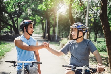 asian boy with friend ride a bike/bicyle at outdoor green park in summer, teamwork concept