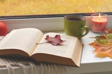 autumn still life. books, leaves, cup and candlestick on window. concept of autumn reading time and romantic, hygge, unplug, mindfulness, warm, cozy seat opened book, rustic style home decor