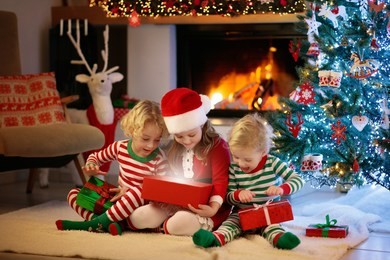 children at christmas tree and fireplace on xmas eve. family with kids celebrating christmas at home. boy and girl in matching pajamas decorating xmas tree and opening presents. holiday gifts for kid.