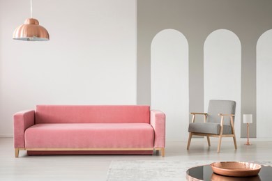 real photo of a creative living room interior decorated with arches, pink sofa and retro armchair