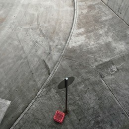 elevated view of section of grey concrete pavement and road with street sign. a single red milk crate adds color.