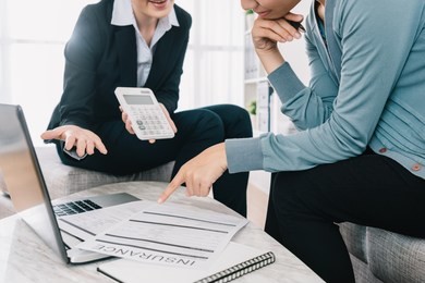 professional insurance agent showing the amount of the insurance case product to the shrewd housewife in the living room. businesswoman holding calculator and introducing the new project.