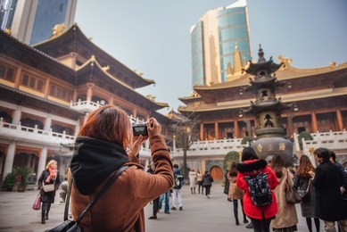 rear view of young woman traveler taking photo picture at temple in china. young asian woman in jacket clothes using camera take a picture of temple in shanghai.
