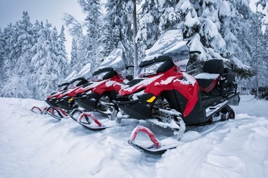 group of four brightly colored red and black snowmobiles are ready for adventure ride. vehicles parked in line near beautiful forest in lapland, finland. heavy snow. winter seasonal landscape.