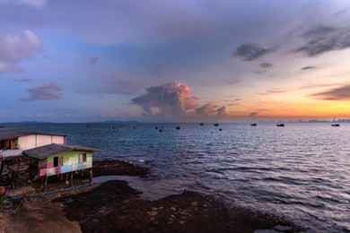 fisherman's house is located at sea with sunrise and white clouds. fishing boat floats in sea with sun shining. view from koh larn, chon buri thailand.