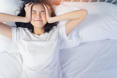 woman stretching in bed after waking up, back view. woman sitting near the big white window while stretching on bed after waking up with sunrise at morning, back view.