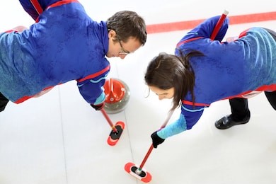 curling games. the player is brushing the ice by directing the stone to the house