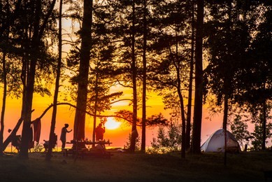 camping on the beach during the sunset with silhouettes of young people, tents and forest trees. picnic and barbecue party outdoors. friends having fun. concept of relaxation, holidays and recreation