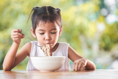 cute asian child girl eating delicious instant noodles with fork in the nature background