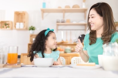 asian children and her mom have a breakfast in the morning, asian mother feeling glad and show thumbs up sign with her hand, child nutrition and development, they feeling happy in family time