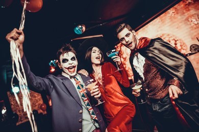 young people drinking cocktails at halloween party. group of young smiling friends wearing halloween costumes drinking cocktails and having fun in nightclub. celebration of halloween