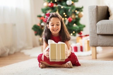 christmas, holidays and childhood concept - happy girl with gift box at home