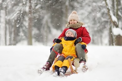little boy and mother sliding in the snow. family winter activities outdoors.