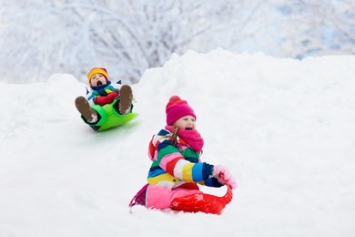 little girl and boy enjoying sleigh ride. child sledding. toddler kid riding a sledge. children play outdoors in snow. kids sled in snowy park in winter. outdoor fun for family christmas vacation.