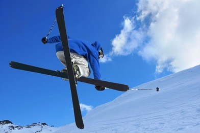 a free style skier performing a high jump. in the background ski lifts in the mountains