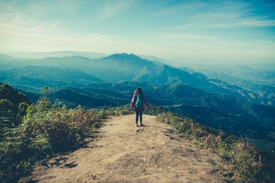 young woman traveler with backpack looking the beautiful scenery mountains view in morning sunrise while trekking on kew mae pan,doi inthanon national park, the top highest mountain of thailand.