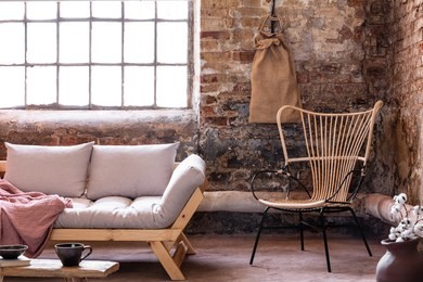 armchair next to grey sofa with cushions in industrial interior with window and red brick wall. real photo