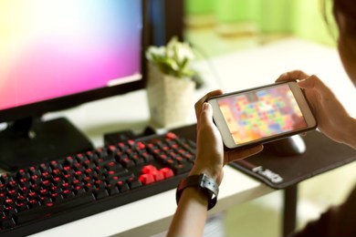 gamer concept. teenage girl gamer playing videogames on smartphone and computer with keyboard red backlit on white pc desk.