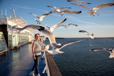 older woman watching seagulls flying. photo of a middle aged lady on the cruise ship deck in a baltic sea cruise.