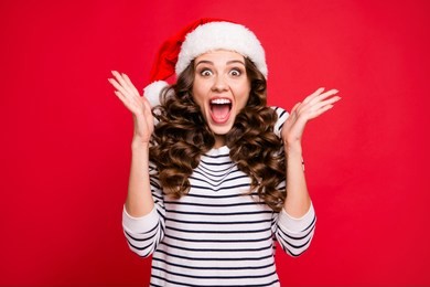 merry holly x mas portrait of crazy cool cheerful glad positive optimistic charming curly-haired girl in casual striped pullover clapping palms waiting for gift isolated over red background