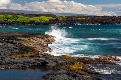 wave crashing on dark lava rocks of black sand beach (punaluu), on the big island of hawaii

