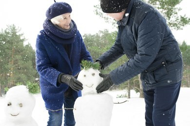 portrait of happy senior couple building snowman while enjoying walk in beautiful winter forest with snow falling gently