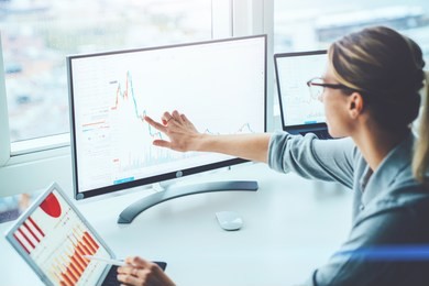 back view of business woman sitting at desktop front pc computer with financial graphs and statistics on monitor. analysis of digital market and investment in block chain crypto currency. stock trade