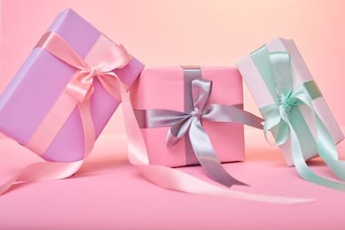 three presents with red bow on pastel trendy pink background with little silver sparkles. flat lay style.