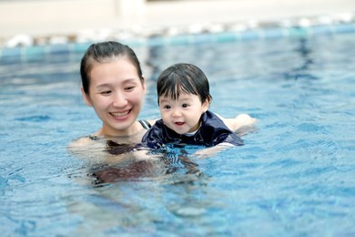 asian mom and baby are swimming in a pool with great happiness