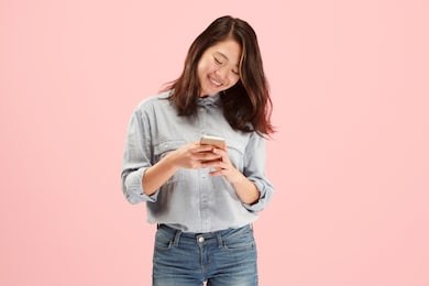 young beautiful woman using mobile phone studio on pink color studio background. human facial emotions concept. trendy colors