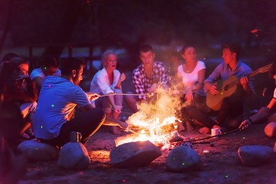 a group of happy young friends relaxing and enjoying  summer evening around campfire on the river bank