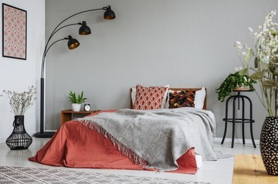 patterned pillow and grey blanket on king size bed with dark orange duvet in luxury bedroom interior in elegant apartment, real photo with copy space on the wall