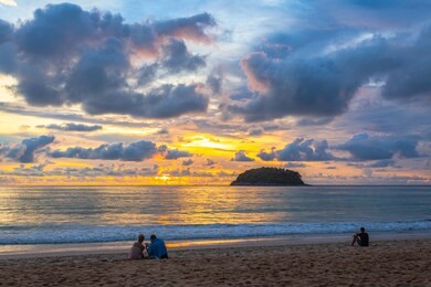 beautiful sunset behind pu island at kata beach phuket. a lot of tourists relax on the beach during sunset.