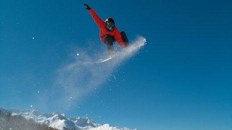 awesome action shot of male snowboarder leaving a trail of snow while doing a spectacular grab trick as he flies through the air. breathtaking shot of a professional athlete snowboarding in the alps.