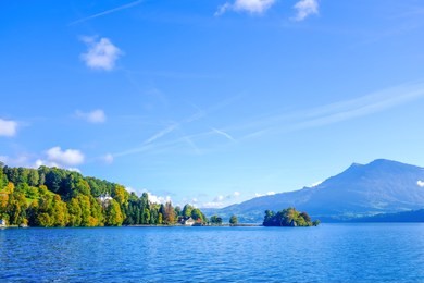 the shoreline from the lake lucerne with mount pilatus in the background on the right side. on the left side is a small hill with green trees. 